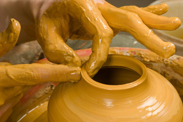 Hands of a potter, creating an earthen jar of yellow clay