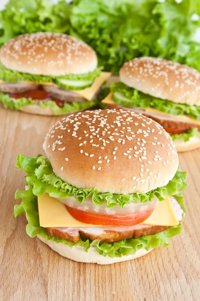 Tři burger s masem a zeleninou na dřevěné desce — Stock fotografie