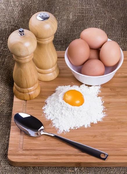 La yema, los huevos de las gallinas de casa, la cuchara, la sal y la pimienta con la harina de trigo en la cocina a la tabla — Foto de Stock