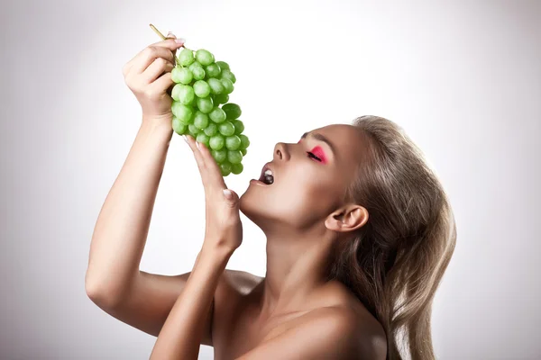 Kaunis nuori nainen syö vihreitä rypäleitä — kuvapankkivalokuva
