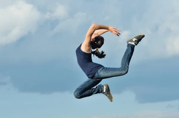 Beautiful girl in gymnastic jump against blue sky — Stock Photo, Image