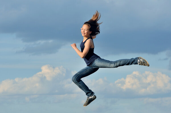 Beautiful girl in gymnastic jump against blue sky