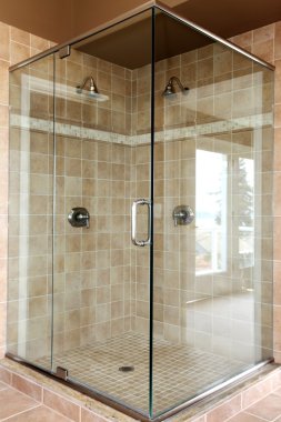 Modern new glass walk in shower with beige tiles.