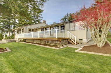 Beige one story house with deck and grass during spring. clipart