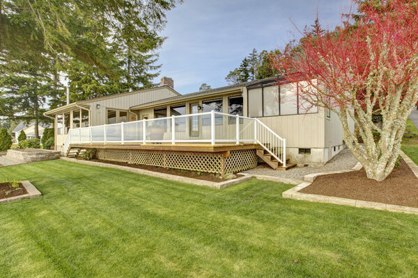 Beige one story house with deck and grass during spring.