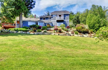 Large blue house with green hill and stone walls. clipart