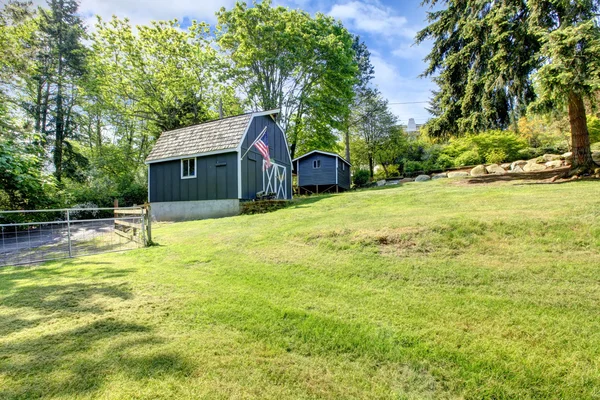 Groot huis met blauwe schuur met gras. — Stockfoto