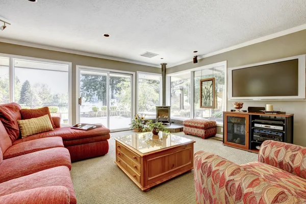 Obývací pokoj s červenou pohovku, béžové zdi a mnoho oken. — Stock fotografie