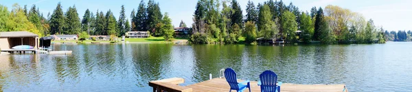 Lake waterfront met pier en blauw stoelen en voorjaar bomen. — Stockfoto