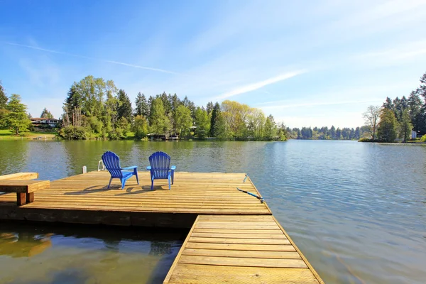 Lake waterfront with pier and two blue chairs. — Stock Photo, Image
