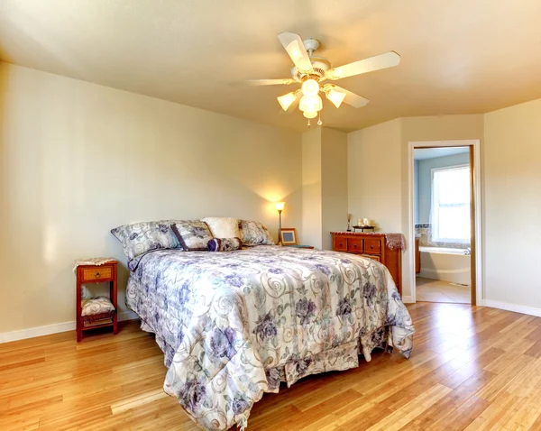Einfaches Schlafzimmer mit blumigem Bettzeug und Hartholzboden. — Stockfoto