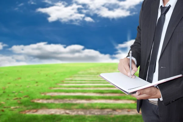 Aziatische zakenman schrijven op een notitieblok op blauwe hemel veld — Stockfoto