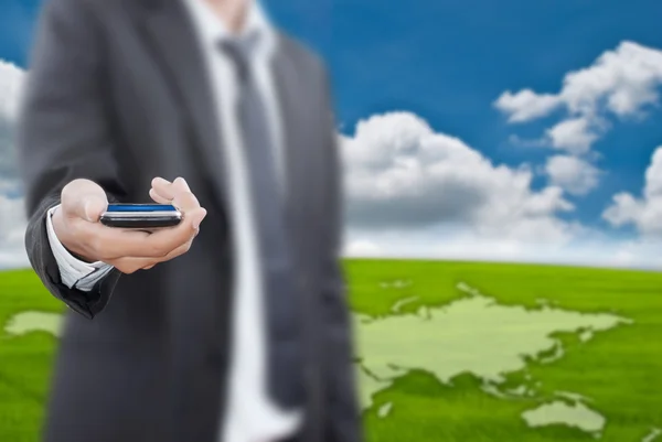 Biznesmen posiadania telefonu komórkowego na niebieski niebo pole — Zdjęcie stockowe