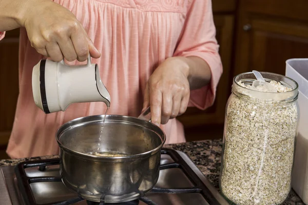 Faire le petit déjeuner avec l'ajout d'eau à la farine d'avoine sur le dessus de la cuisinière — Photo