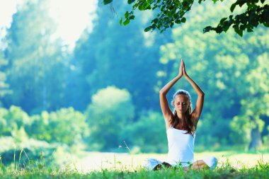 Young woman doing yoga exercise in green park clipart