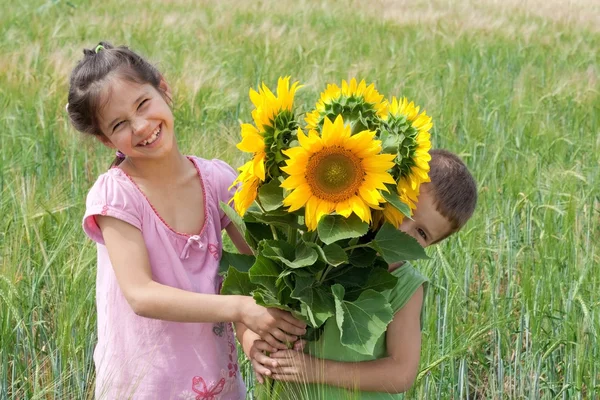 Dwoje dzieci z słoneczniki w polu pszenicy — Zdjęcie stockowe