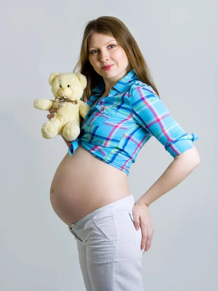 Mujer embarazada acariciando su vientre con un oso en la mano y c —  Fotos de Stock