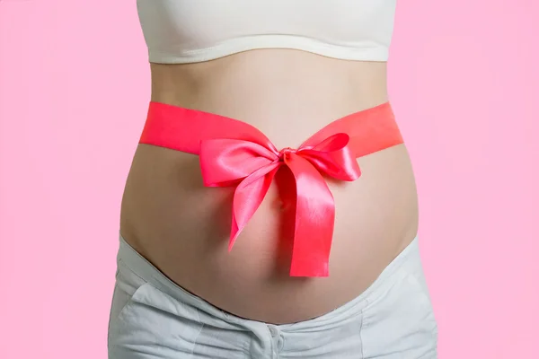 Όμορφη νεαρή έγκυο γυναίκα με κορδέλα. απομονώνονται σε ροζ bac — Φωτογραφία Αρχείου