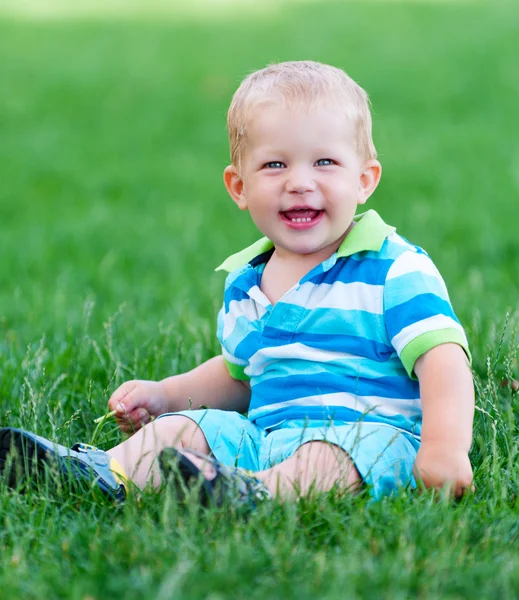 Маленький мальчик сидит на зеленой лужайке — стоковое фото