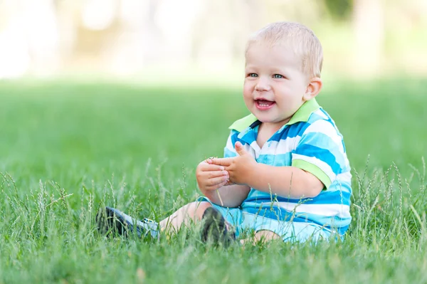 Счастливый мальчик, сидящий на зеленом ковре — стоковое фото