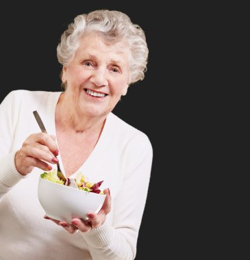 siyah arka plan üzerinde salata yiyen kadın kıdemli portresi