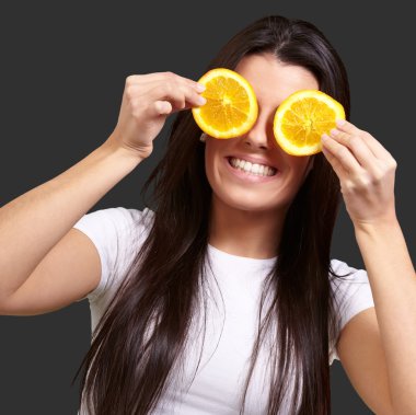 Portrait of young woman holding orange slices in front of her ey clipart