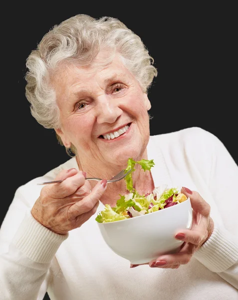 Portrait of senior woman eating a fresh salad over black backgro — Stock Photo, Image