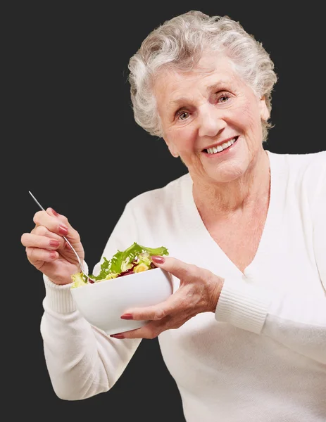 Portrét starší ženy jíst salát černém pozadí — Stock fotografie