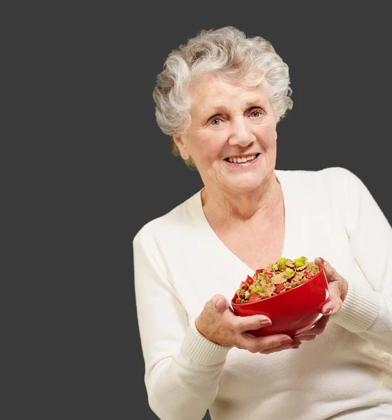 Portrait of healthy senior woman holding cereals bowl over black — Stock Photo, Image