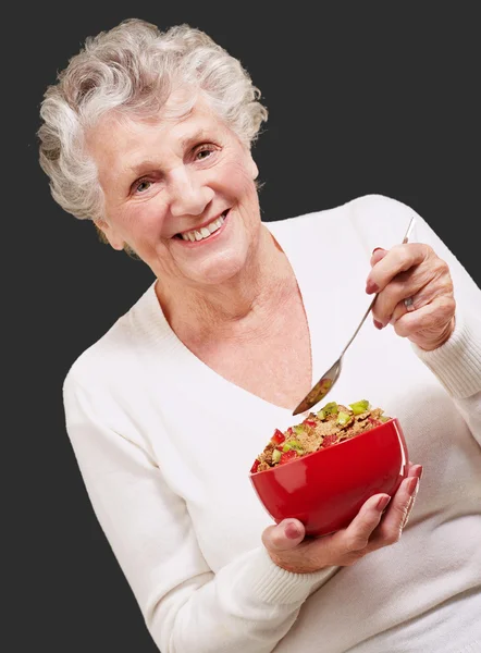Portrait of senior woman holding a cereals bowl against a black — Stock Photo, Image