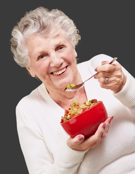 Portrait of senior woman holding a cereals bowl against a black — Stock Photo, Image