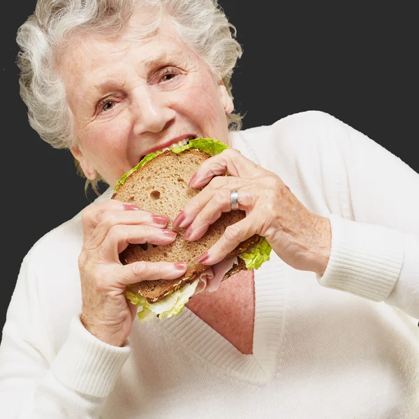 Porträt einer Seniorin, die auf schwarzem Rücken ein vegetarisches Sandwich isst — Stockfoto