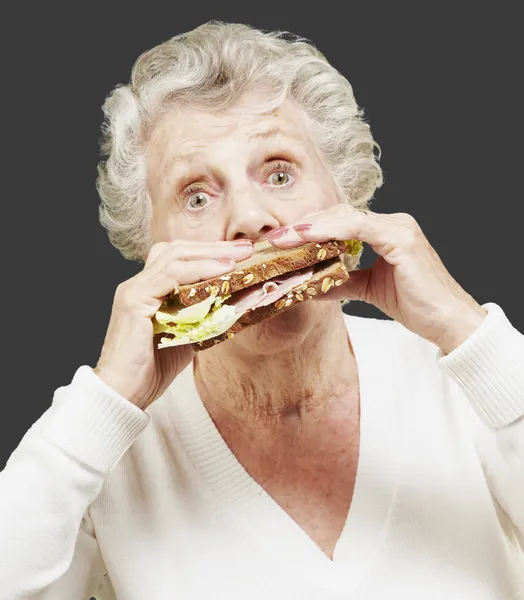 Senior woman eating a healthy sandwich against a black backgroun — Stock Photo, Image