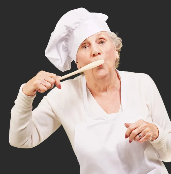 Retrato de cocinera mujer mayor con cuchara de madera en la boca sobre bl —  Fotos de Stock