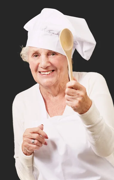Πορτρέτο του ανώτερος μάγειρας γυναίκα που κρατά ένα ξύλινο κουτάλι πάνω από το μαύρο — Φωτογραφία Αρχείου