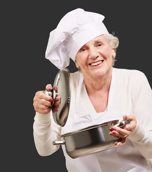 Portrait of cook senior woman opening sauce pan over black — Stock Photo, Image