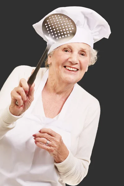 Porträt der süßen Senior-Köchin, die einen Metalllöffel über b hält — Stockfoto