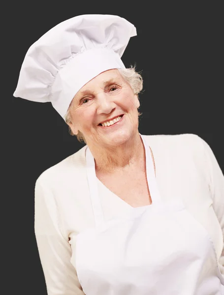 Porträtt av cook senior kvinna ler över svart bakgrund — Stockfoto