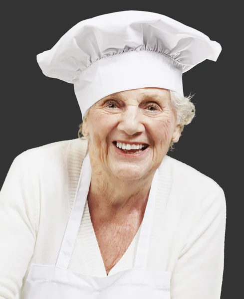 Mulher sênior cozinheiro segurando uma tigela com salada contra uma parte traseira preta — Fotografia de Stock