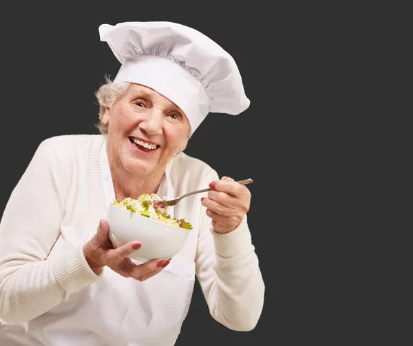 Ritratto di anziana cuoca mangiare insalata su nero — Foto Stock