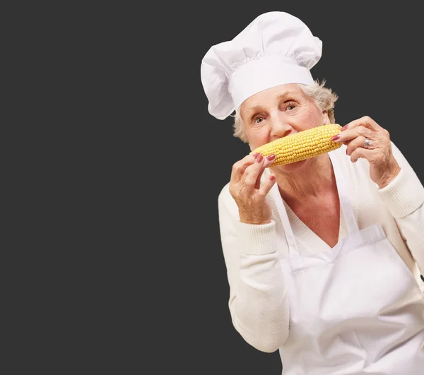 Portrait of senior cook woman eating corn cob over black backgro — Stock Photo, Image