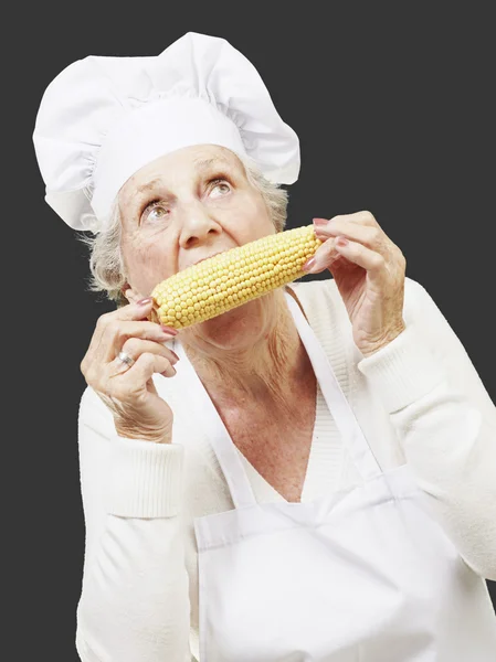 上了年纪的女厨师在黑背景下吃玉米芯 — 图库照片