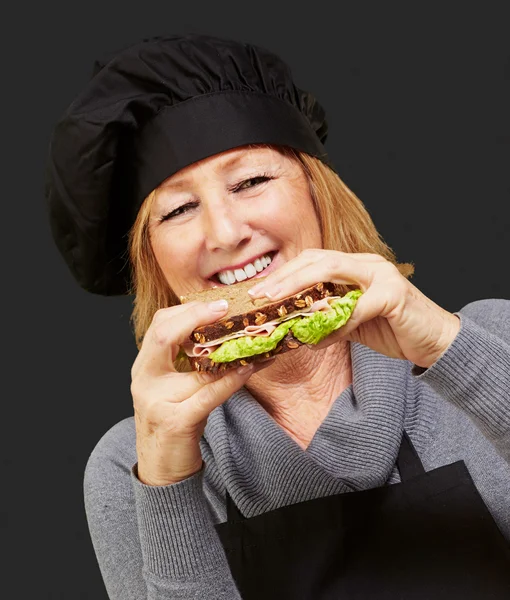 Bitkisel bir sandviç siyah bac üzerinde tutan orta yaşlı aşçı kadın — Stok fotoğraf