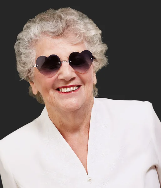 Retrato de mulher idosa feliz usando óculos de coração sobre preto — Fotografia de Stock