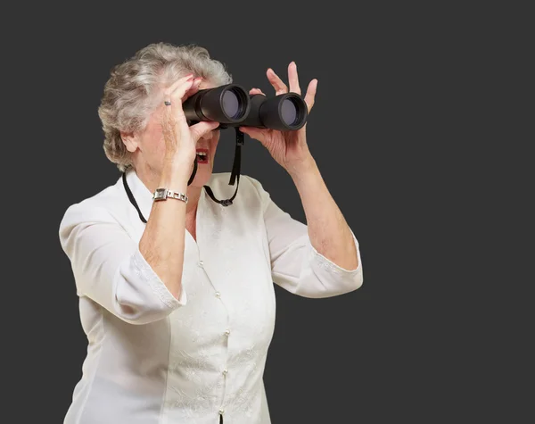 Portrait of senior woman looking through a binoculars over black — Stock Photo, Image