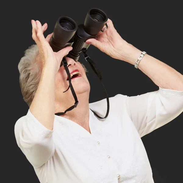 Portrait of senior woman looking through a binoculars over black — Stock Photo, Image