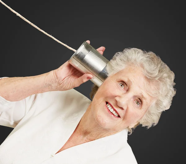Portrait of senior woman hearing with metal tin can over black b — Stock Photo, Image