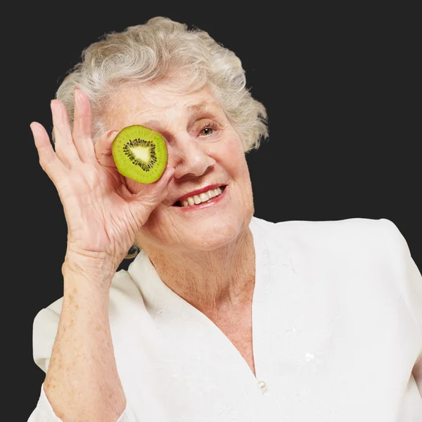 Portret van senior vrouw bedrijf kiwi voor haar oog over b — Stockfoto