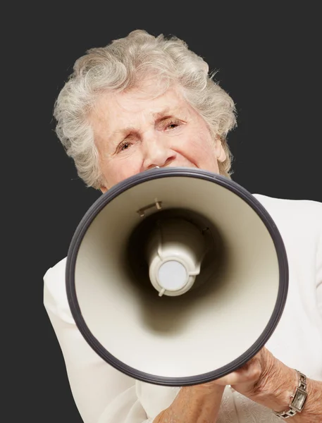 Портрет пожилой женщины, кричащей с мегафоном над черным пляжем — стоковое фото