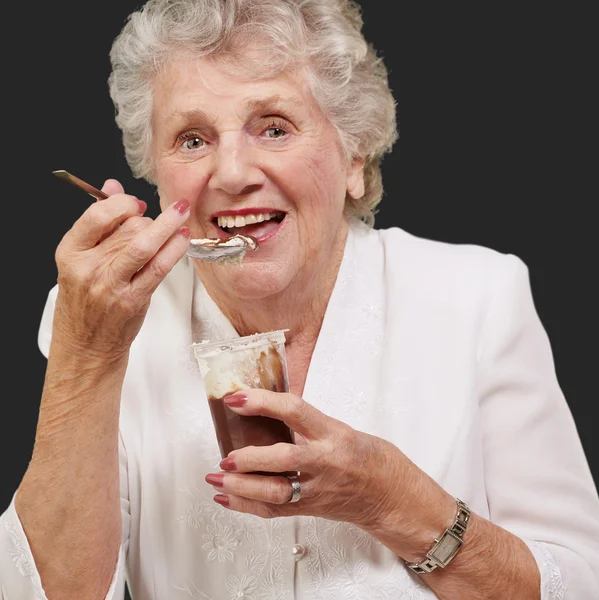 Retrato de mulher idosa comendo chocolate e xícara de creme sobre bla — Fotografia de Stock